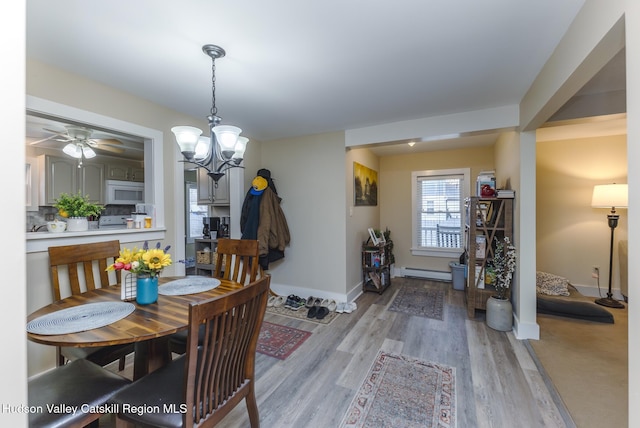 dining area with light wood-type flooring, a baseboard heating unit, and ceiling fan with notable chandelier