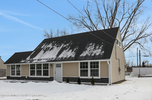 view of front of property with stone siding, roof with shingles, and fence