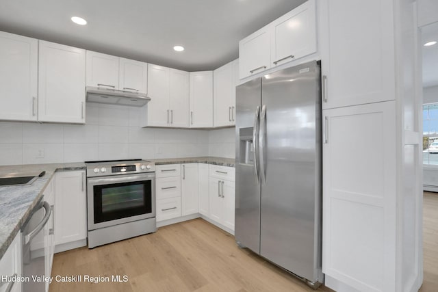 kitchen with under cabinet range hood, stainless steel appliances, white cabinetry, light stone countertops, and light wood finished floors