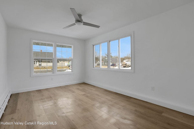 spare room featuring a baseboard heating unit, ceiling fan, light wood-style flooring, and baseboards