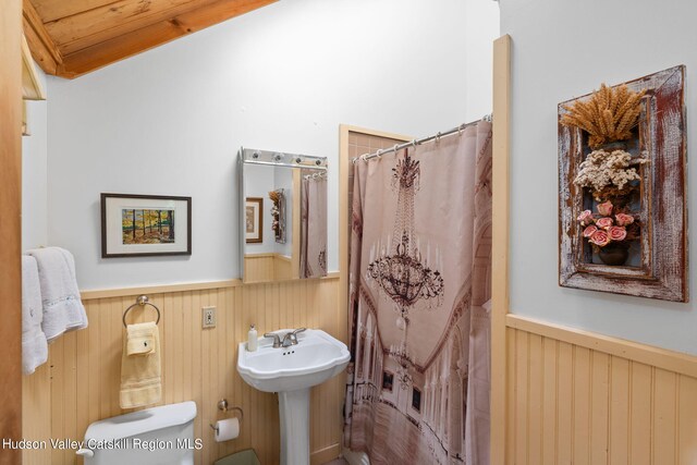 bathroom featuring a shower with curtain, vaulted ceiling, toilet, and wood walls