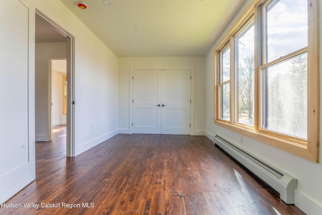 unfurnished bedroom featuring a baseboard heating unit, dark wood-style flooring, a closet, and baseboards