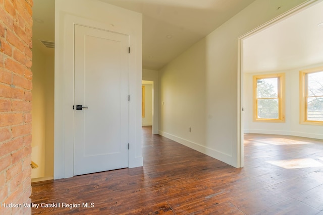 corridor featuring brick wall, visible vents, baseboards, and hardwood / wood-style flooring