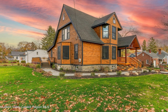 back of house featuring a deck, a lawn, and roof with shingles