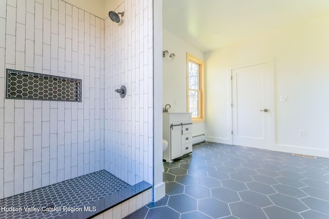 full bath featuring toilet, a baseboard heating unit, a tile shower, baseboards, and tile patterned floors