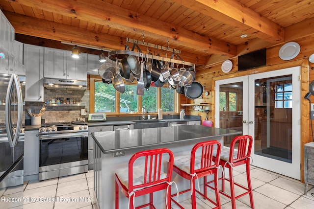 kitchen with appliances with stainless steel finishes, wooden walls, light tile patterned floors, a kitchen island, and range hood