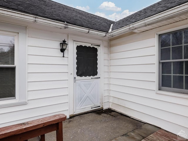 view of exterior entry with roof with shingles