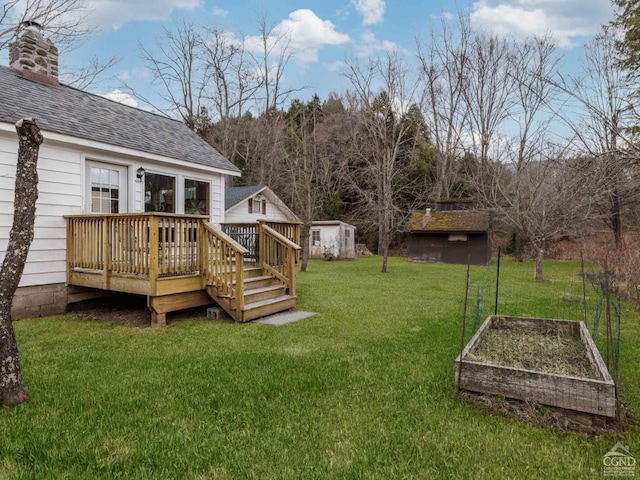 view of grassy yard featuring a vegetable garden, a deck, a shed, and an outbuilding
