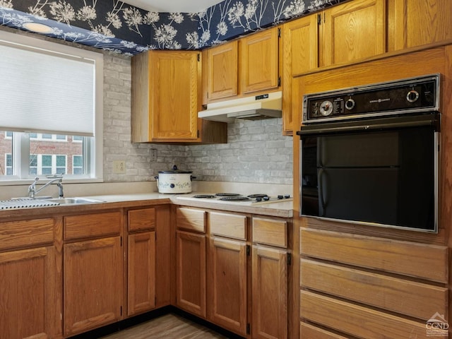 kitchen featuring oven, under cabinet range hood, a sink, light countertops, and brown cabinetry
