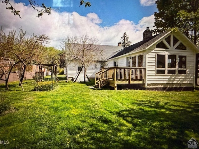 back of property featuring a deck, a yard, and a chimney
