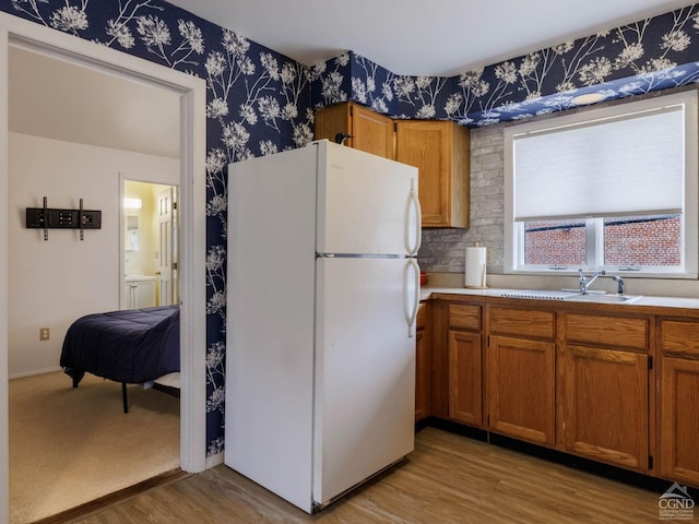 kitchen with freestanding refrigerator, brown cabinets, wallpapered walls, light countertops, and light wood-style flooring