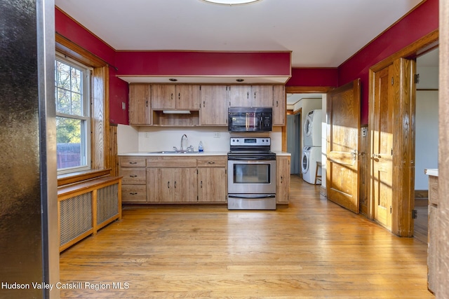 kitchen with radiator heating unit, sink, light hardwood / wood-style flooring, stacked washer / drying machine, and electric stove
