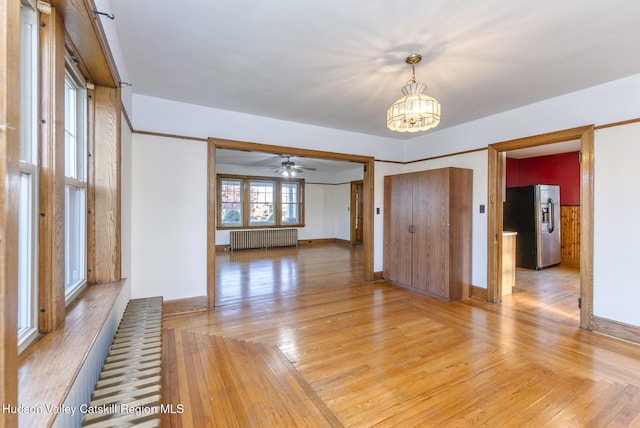 empty room with ceiling fan with notable chandelier, radiator heating unit, and light hardwood / wood-style flooring