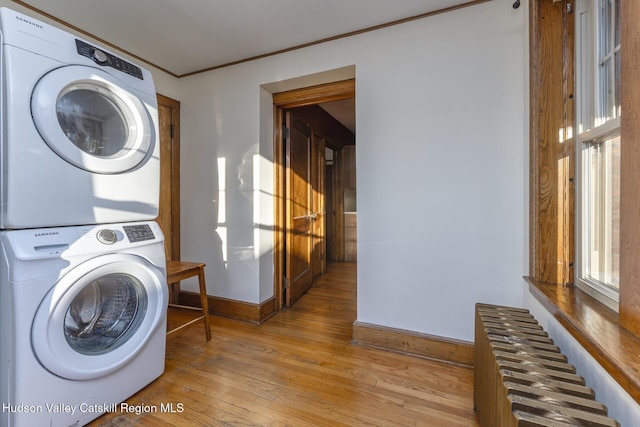 laundry area featuring radiator heating unit, light wood-type flooring, and stacked washer / drying machine