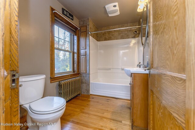 full bathroom with vanity, radiator, tiled shower / bath, toilet, and wood-type flooring