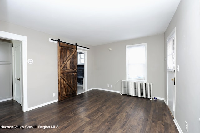 empty room featuring radiator, wood finished floors, baseboards, and a barn door