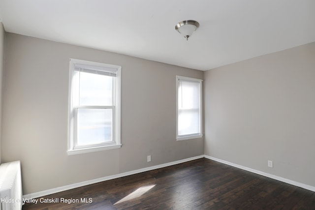 empty room featuring baseboards, radiator heating unit, and dark wood finished floors