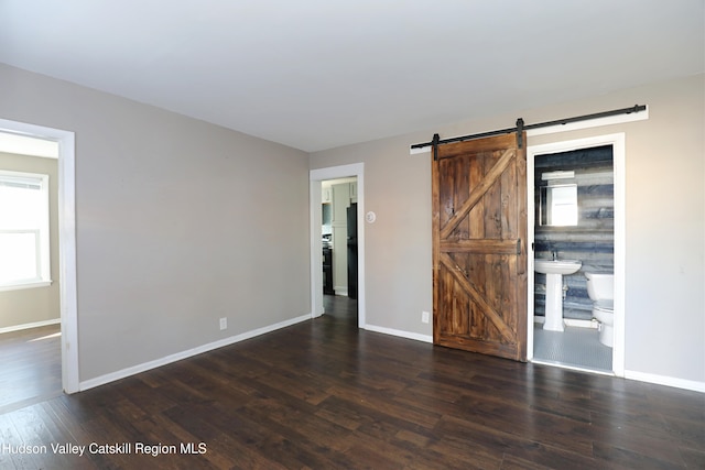 empty room featuring wood finished floors, baseboards, and a barn door