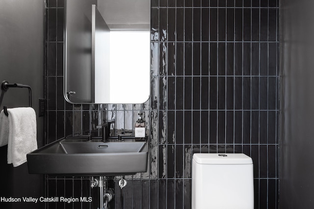 bathroom featuring toilet, tile walls, decorative backsplash, and a sink