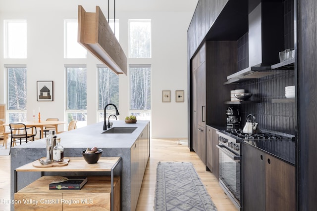 kitchen featuring wall chimney exhaust hood, modern cabinets, high end range, and a sink