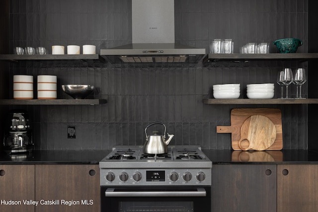 kitchen with dark countertops, stainless steel gas stove, wall chimney exhaust hood, and open shelves