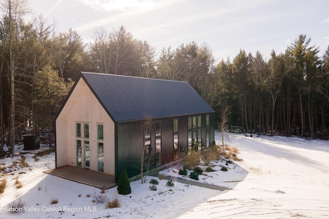 snow covered structure with a forest view and central AC unit