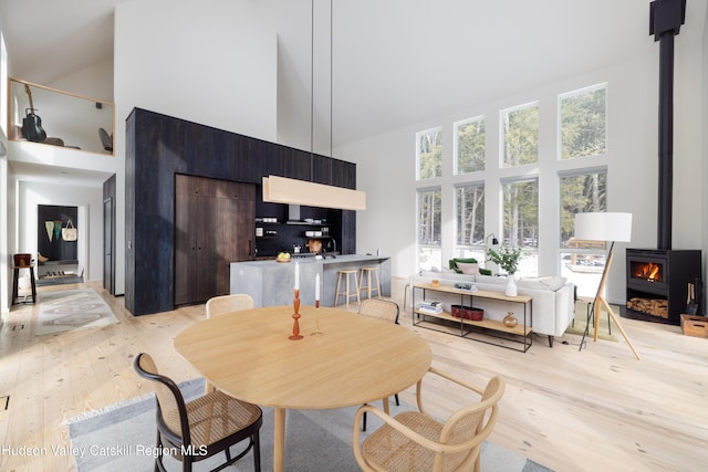 dining area featuring a wood stove, light wood-style floors, and high vaulted ceiling