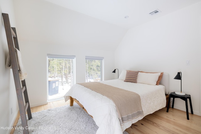 bedroom featuring access to exterior, visible vents, vaulted ceiling, and wood finished floors