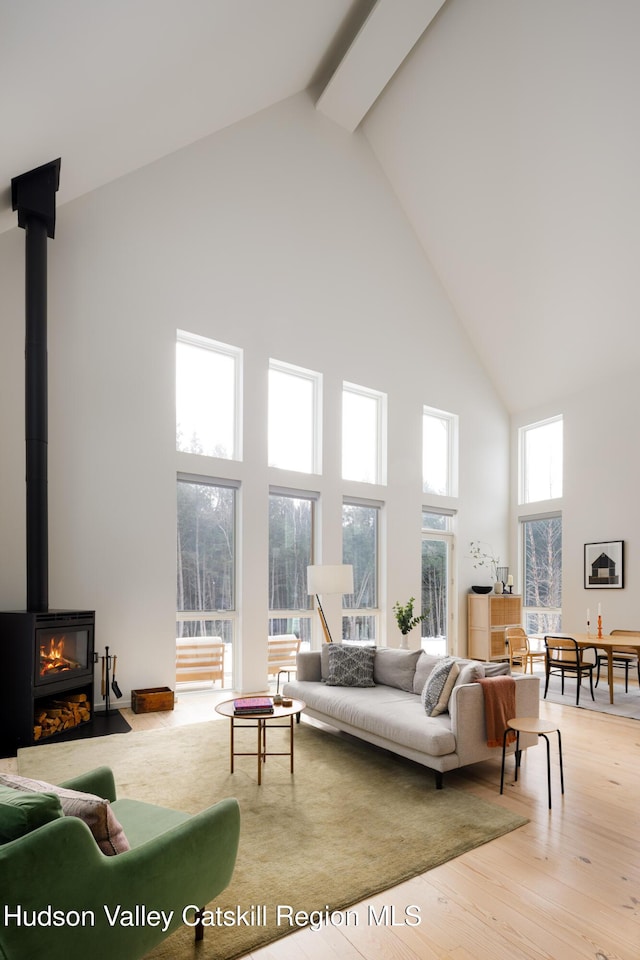 living area featuring high vaulted ceiling, beamed ceiling, wood finished floors, and a wood stove