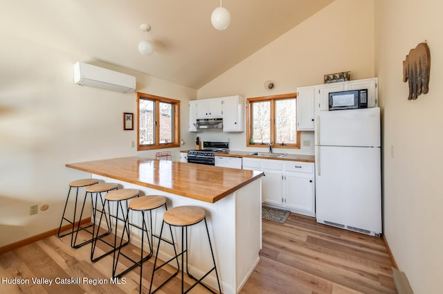 kitchen with white cabinetry, a wall mounted air conditioner, a breakfast bar area, black appliances, and light wood-type flooring