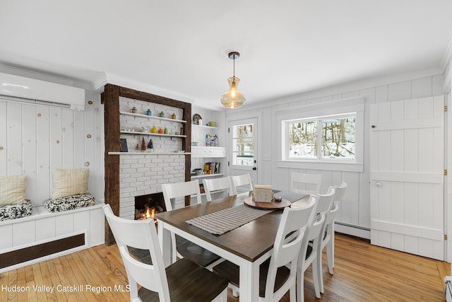 dining space featuring light wood-type flooring, a wall unit AC, a baseboard radiator, and a brick fireplace