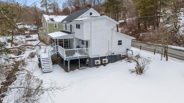 snow covered house featuring a chimney, stairway, and a wooden deck