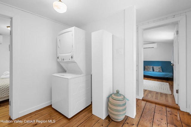 laundry room with baseboards, light wood finished floors, a wall mounted AC, and stacked washer / drying machine