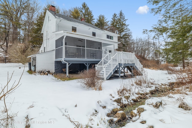 snow covered rear of property with a chimney, stairway, a sunroom, ceiling fan, and a deck