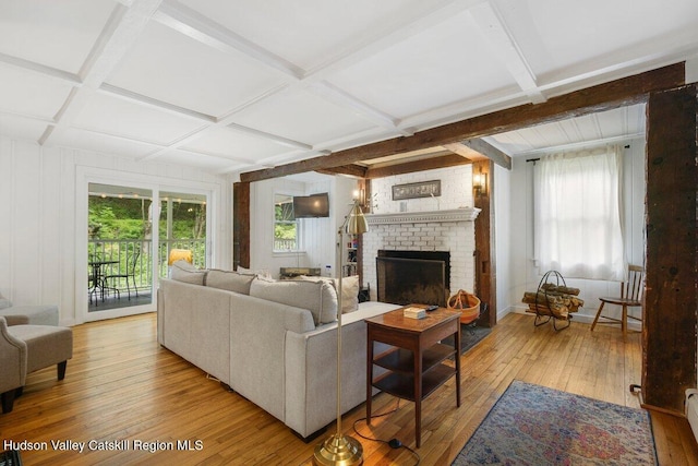 living room featuring coffered ceiling, beamed ceiling, a baseboard radiator, light wood-style flooring, and a brick fireplace