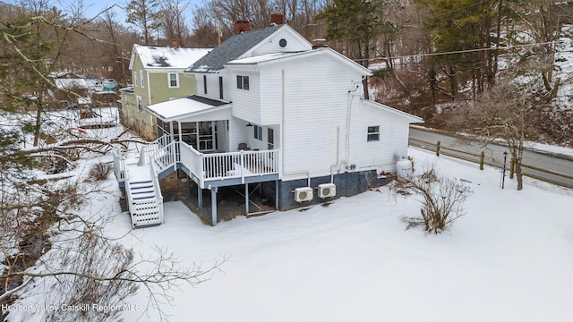 snow covered back of property with stairs, a deck, a chimney, and a sunroom