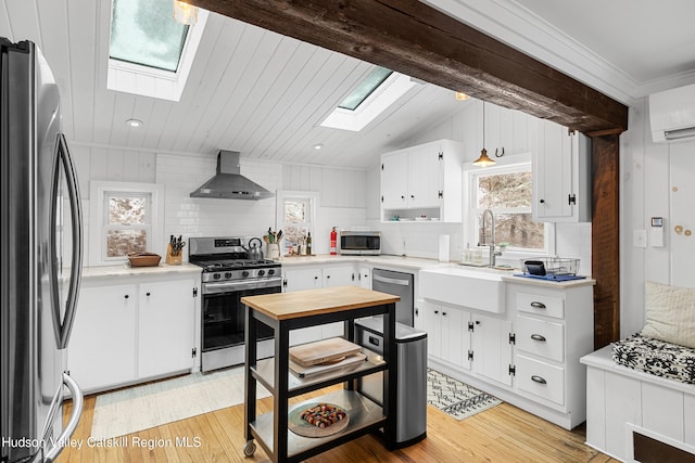 kitchen with stainless steel appliances, light countertops, wall chimney exhaust hood, and white cabinetry