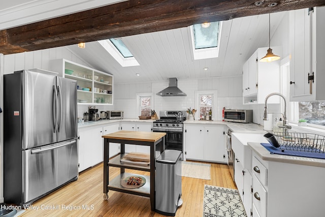 kitchen with wall chimney range hood, white cabinets, light countertops, backsplash, and appliances with stainless steel finishes