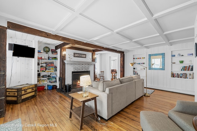 living area featuring coffered ceiling, light wood-style flooring, a brick fireplace, built in shelves, and beam ceiling