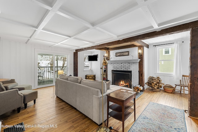 living area featuring a brick fireplace, light wood-style flooring, coffered ceiling, and beamed ceiling