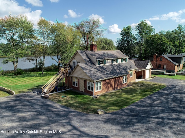 exterior space with stairway, a chimney, a detached garage, brick siding, and a front yard