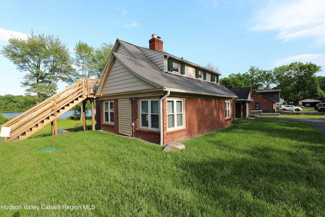view of side of home featuring brick siding, a chimney, a yard, roof with shingles, and stairs