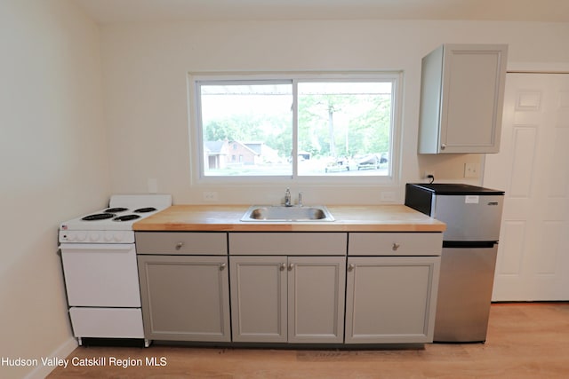 kitchen with white electric range oven, a sink, light wood-style floors, gray cabinetry, and freestanding refrigerator