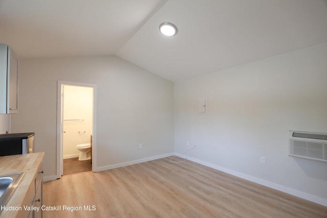 interior space featuring light wood-style flooring, a sink, baseboards, a wall mounted air conditioner, and lofted ceiling
