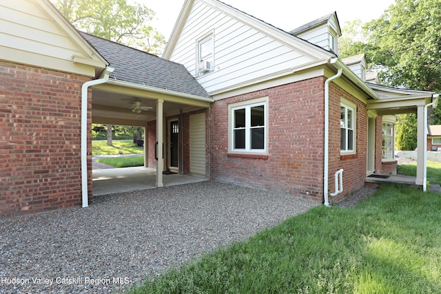 view of home's exterior featuring ceiling fan, a shingled roof, brick siding, and a yard