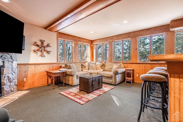 carpeted living room with wainscoting, beam ceiling, recessed lighting, wood walls, and a stone fireplace