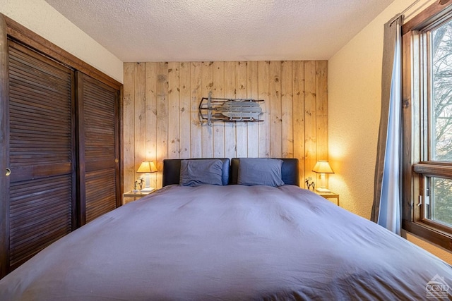 bedroom with wooden walls, a closet, multiple windows, and a textured ceiling