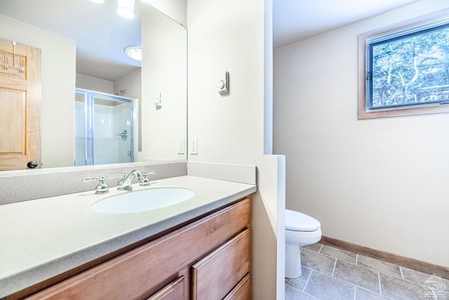 bathroom with a shower stall, vanity, baseboards, toilet, and stone finish floors
