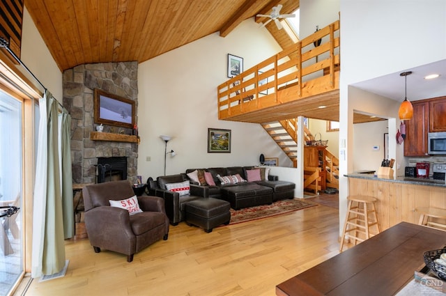living room with stairway, light wood-style flooring, a stone fireplace, wood ceiling, and beam ceiling