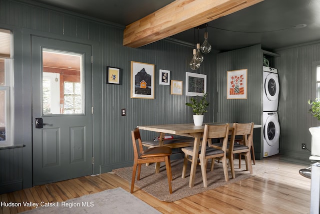 dining area featuring beamed ceiling, stacked washer / drying machine, and light wood-type flooring